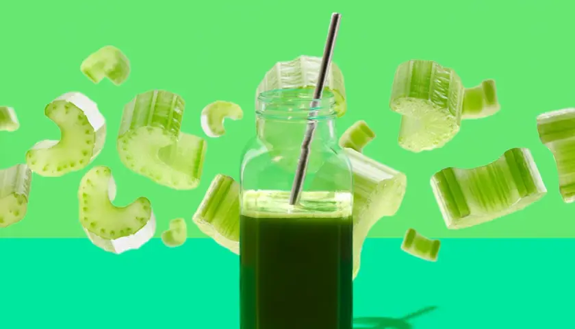 Ein Glas Selleriesaft mit einem Strohhalm, umgeben von schwebenden Selleriestücken. Die Selleriesaft Wirkung wird hier visuell dargestellt.