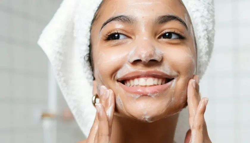 Mujer sonriente con espuma en el rostro, disfrutando de su rutina de doble limpieza facial.