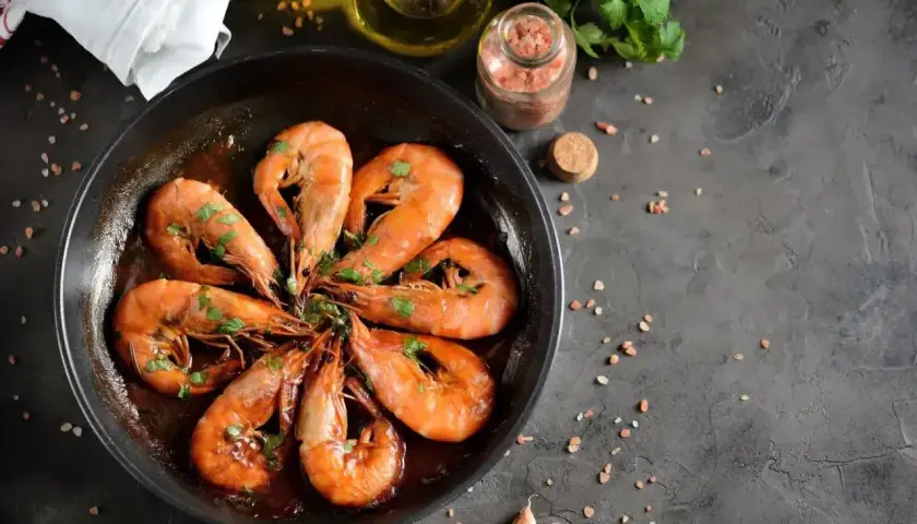 Pyszne krewetki w sosie, część dania frutti di mare, skropione natką pietruszki, gotowe do podania.