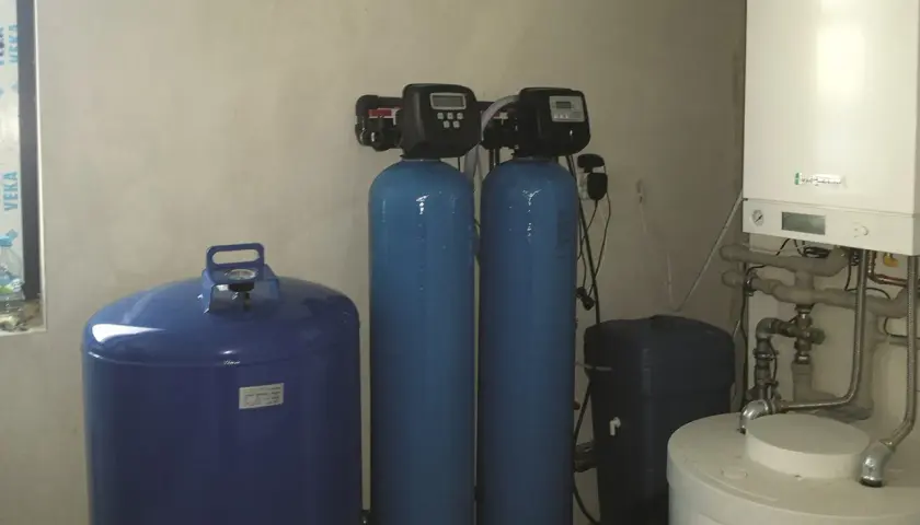 System do uzdatniania wody: niebieski zbiornik, dwa pionowe cylindry z panelami sterowania i biały bojler.