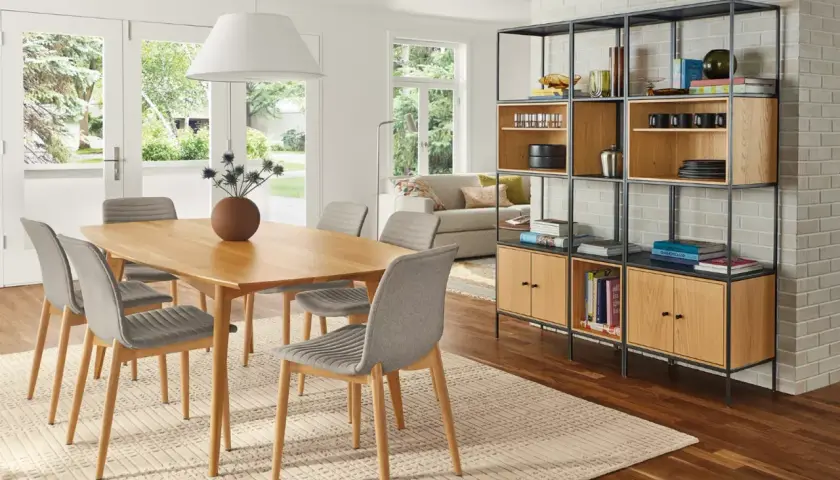 Open living and dining room ideas: a light wood table with grey chairs, a modern shelving unit, and a sofa visible through French doors.