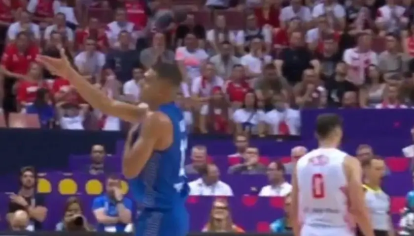 Koszykarz w niebieskim stroju gestykuluje na tle trybun, gdzie widać kibiców w biało-czerwonych barwach. Mecz Izrael Polska.