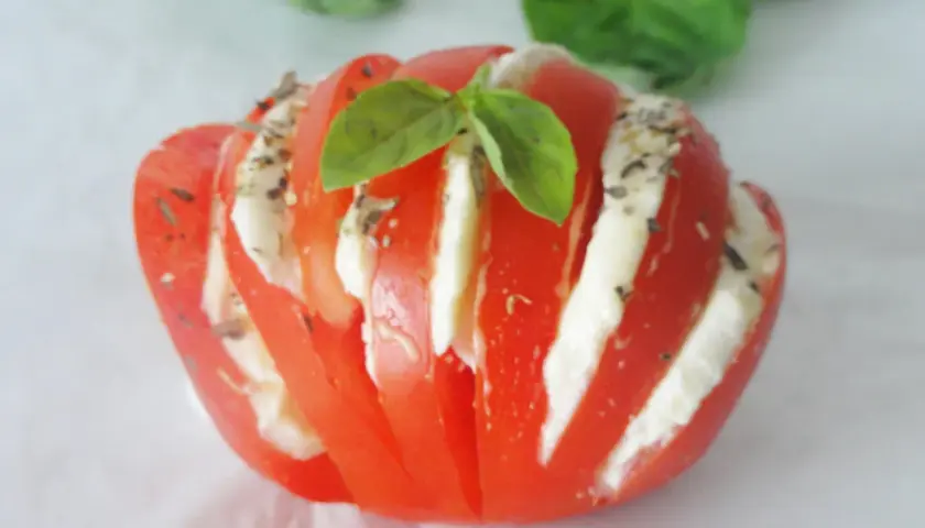 Tomate farcie d'une délicieuse recette avec mozzarella, garnie de basilic frais et d'herbes. Une bouchée d'été parfaite.