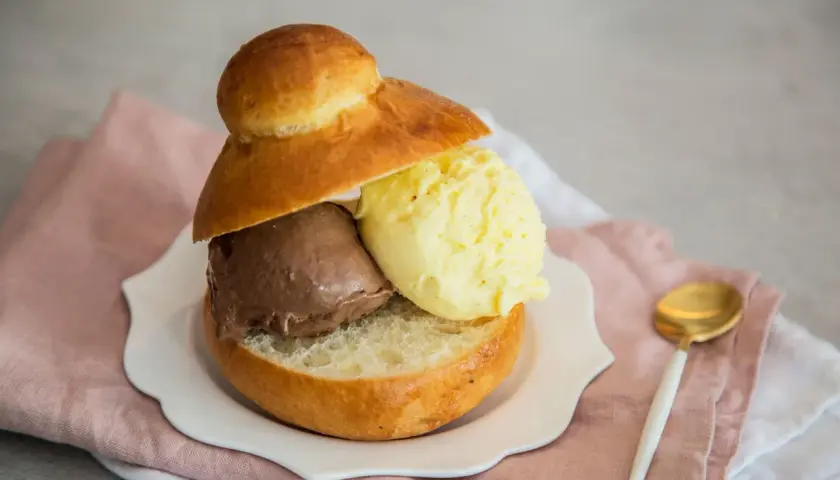 Pyszne lody w bułce: czekoladowe i waniliowe, podane na talerzyku z różową serwetką.