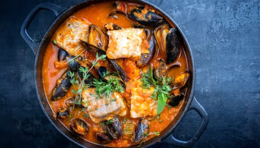 Una ricca zuppa di pesce in una pentola di ghisa, con pezzi di pesce bianco, cozze e erbe aromatiche fresche.