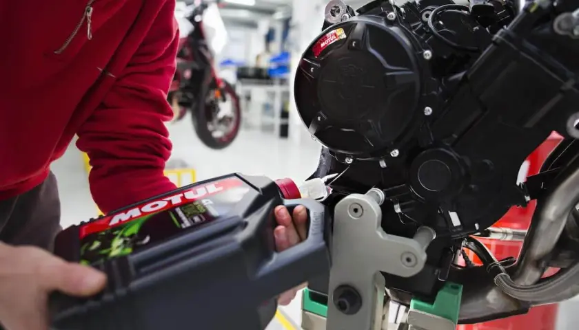 Osoba w czerwonej bluzie nalewa olej Motul do silnika motocykla. Pamiętaj, co ile wymieniać olej w motocyklu, by zapewnić mu długą żywotność.