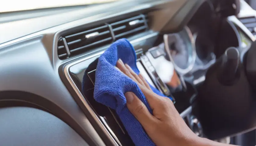 Mano che pulisce il cruscotto dell'auto con un panno blu. Una guida su come pulire il cruscotto della macchina per mantenerlo splendente.
