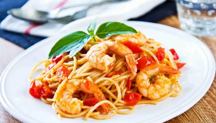Un piatto invitante di pasta con gamberetti e pomodorini, guarnito con basilico fresco.