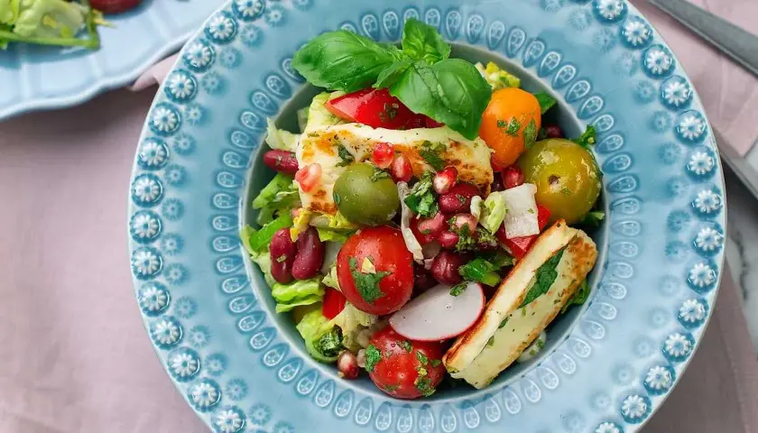 En färgstark sallad med grillad halloumi, tomater, oliver, bönor och granatäpple. Ett perfekt sallad recept för en lätt lunch.