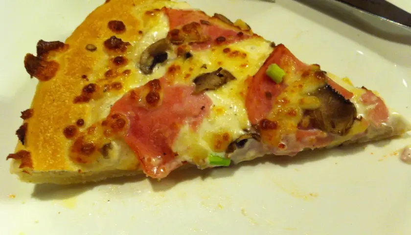 Kawałek pizzy z szynką i pieczarkami, idealny na festiwal pizzy, który trwa do jutra.