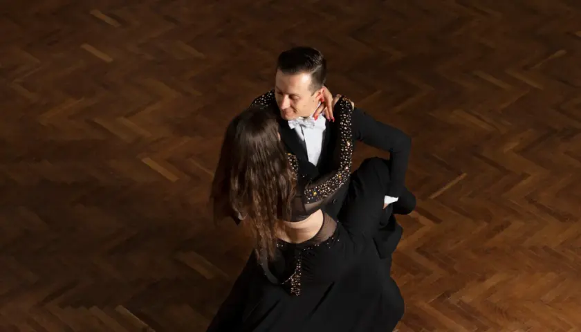 Para tańczy tango argentyńskie, wykonując skomplikowane kroki na drewnianym parkiecie.