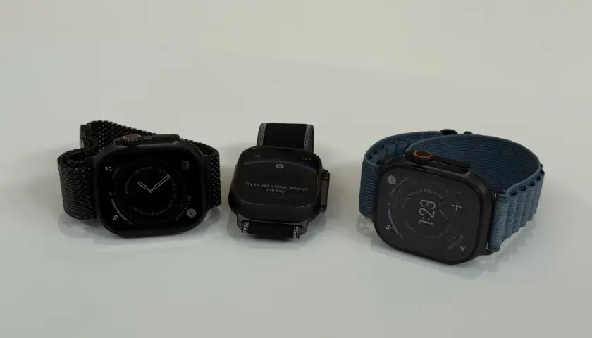 Trzy zegarki Apple Watch na białym tle: jeden z czarną bransoletą, drugi z czarną, trzeci z niebieską.