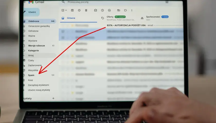 Laptop z otwartym mailem Gmail, zaznaczony folder "Spam" i czerwona strzałka wskazująca na temat maila "ESTA - AUTORYZACJA PODÓŻY USA".