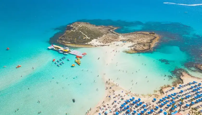 Widok z lotu ptaka na turkusową zatokę z plażą, leżakami i ludźmi kąpiącymi się w morzu.