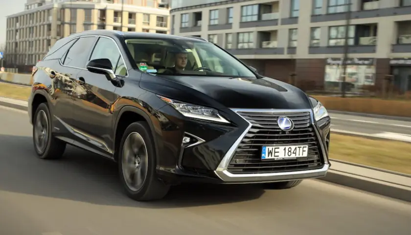 Czarny Lexus RX 450h jedzie ulicą w mieście, za nim widać nowoczesne budynki.