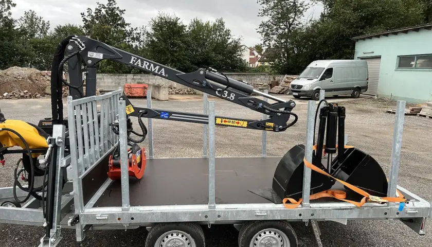 Ein FARMA forstkran für PKW-Anhänger, beladen mit Baggerschaufel und Rüttelplatte, bereit für den Einsatz.