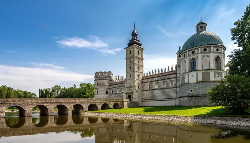 Zamek w Krasiczynie, majestatyczna budowla z wieżą i kopułą, odbija się w spokojnej tafli wody.