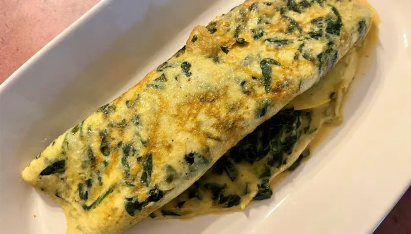 Une omelette aux épinards, dorée et moelleuse, servie sur une assiette blanche. Un délice simple et sain.