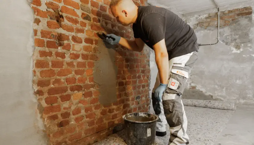 Mann verputzt feuchte Kellerwand.