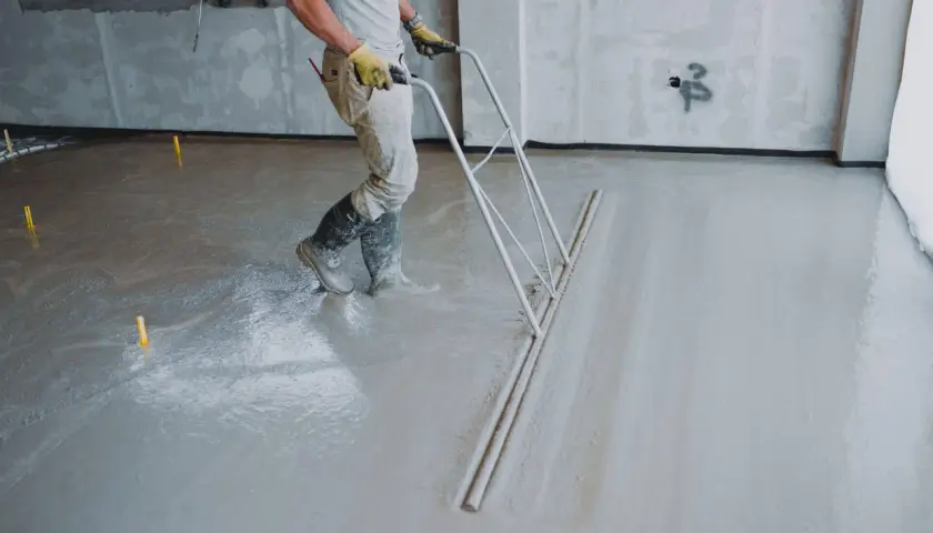 Robotnik wyrównuje świeżą wylewkę betonową. Sprawdź wylewka betonowa cena za m2 robocizny bez materiału.