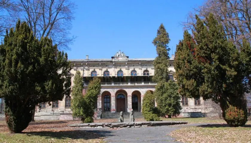 Dawny pałac, otoczony drzewami, z widoczną **promną** fasadą i arkadowym wejściem.