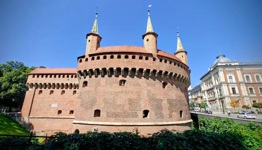 Krakowski zabytek przy Bramie Floriańskiej, okrągła baszta obronna z cegły, góruje nad zielonymi terenami i ulicą.
