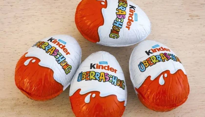 Cztery jajka Kinder Niespodzianka w pomarańczowo-białych opakowaniach na drewnianym tle.