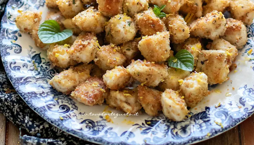 Bocconcini di pollo dorati e croccanti, guarniti con scorza di limone e foglie di menta fresca, serviti su un piatto decorato.