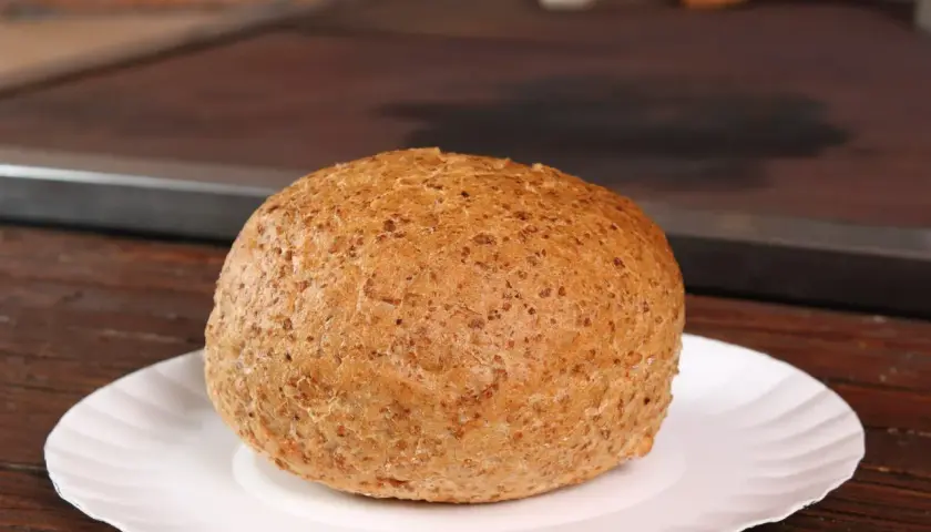 Złocista bułka pełnoziarnista na białym talerzyku. Zastanawiasz się, ile waży bułka? Ta wygląda na idealną na śniadanie.