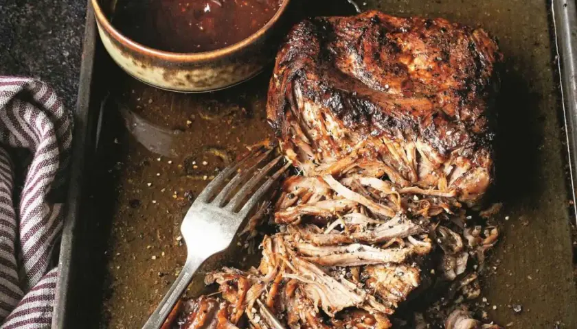 Soczysta, szarpana wieprzowina z sosem barbecue na blasze. Widoczne widelce ułatwiające rozrywanie mięsa.