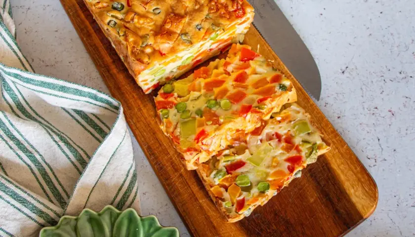 Tranches colorées d'une terrine de légumes savoureuse, garnie de poivrons, carottes et petits pois, prête à être dégustée.