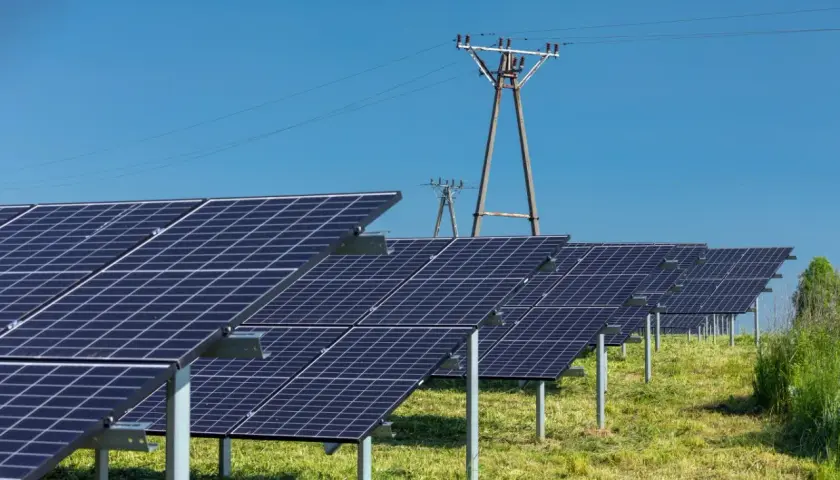 Rzędy paneli fotowoltaicznych na zielonej łące, pod błękitnym niebem. Idealny dzień, kiedy fotowoltaika produkuje najwięcej energii.