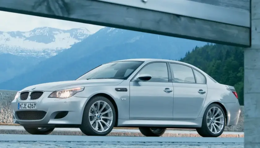 Un elegante BMW M5 E60 plateado descansa ante un paisaje montañoso nevado, listo para la aventura.