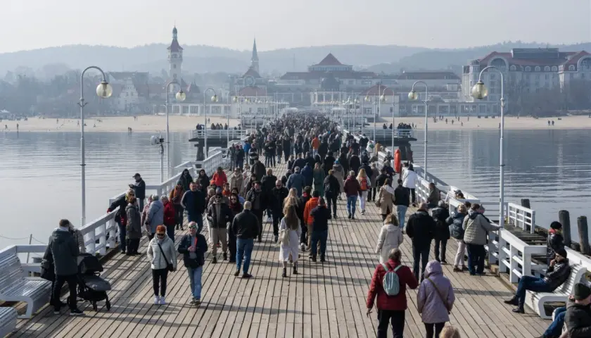 Tłum ludzi spaceruje po najdłuższym molo w Polsce, podziwiając widok na morze i nadmorskie budynki.