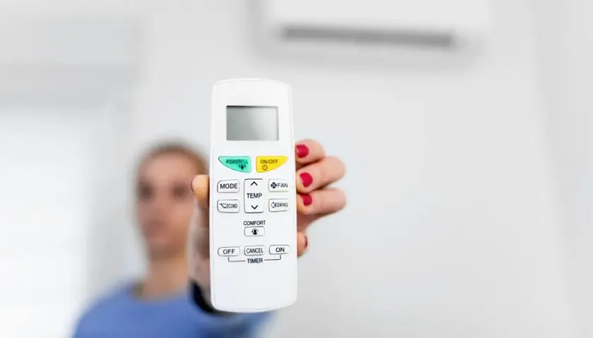 Mano sostiene control remoto de aire acondicionado, listo para activar el símbolo del frío y disfrutar de un ambiente fresco.