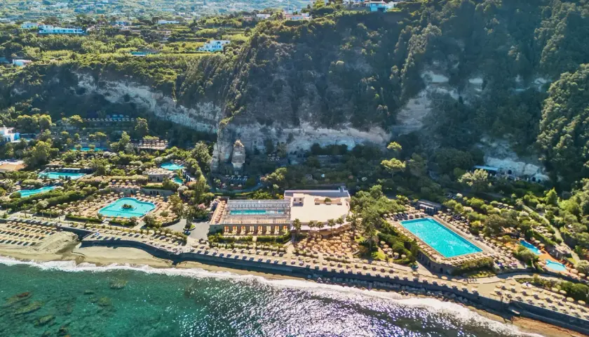 Vista aerea di lussuosi complessi termali a Ischia, con piscine scintillanti, lettini e vegetazione rigogliosa che si affacciano sul mare.