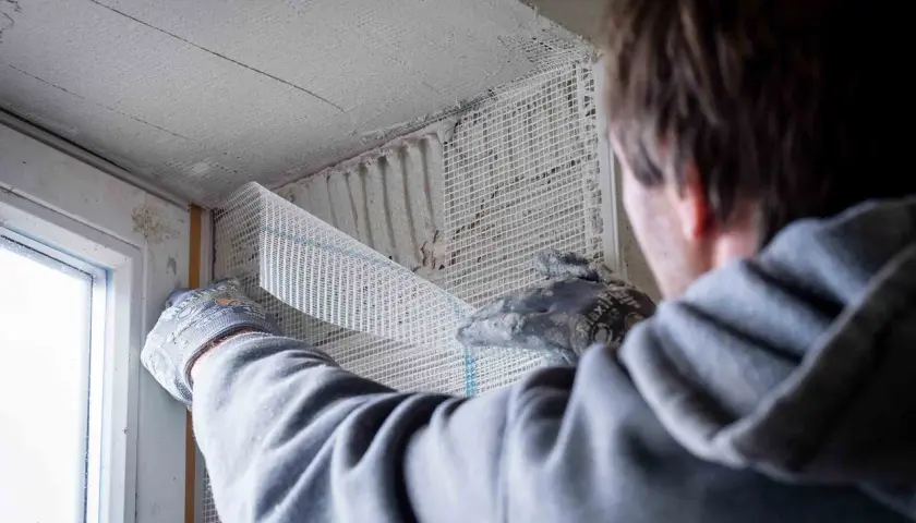 Hand mit Handschuh verputzt Fensterlaibung mit Armierungsgewebe.