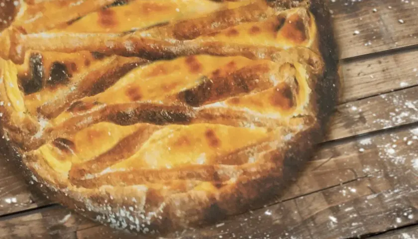 Une tarte au libouli dorée, aux croisillons de pâte bien cuits, repose sur un fond de bois rustique saupoudré de farine.