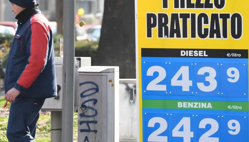 Prezzo praticato per la benzina: 2,429 €/litro. Un uomo in divisa osserva il cartello.