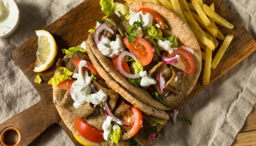 Pyszny grecki gyros z kawałków mięsa opiekanego na rożnie, podany z frytkami, warzywami i sosem.