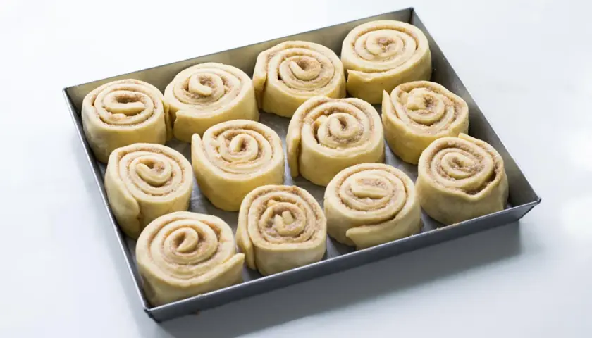 Rotolini alla cannella e mela pronti per essere infornati, disposti in una teglia.