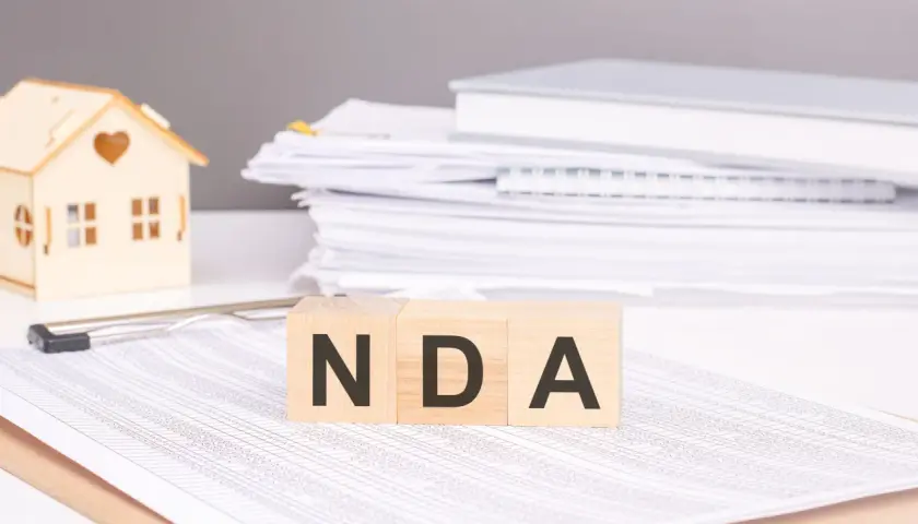 Cubos de madera con las letras NDA, una casa de juguete y pilas de documentos.