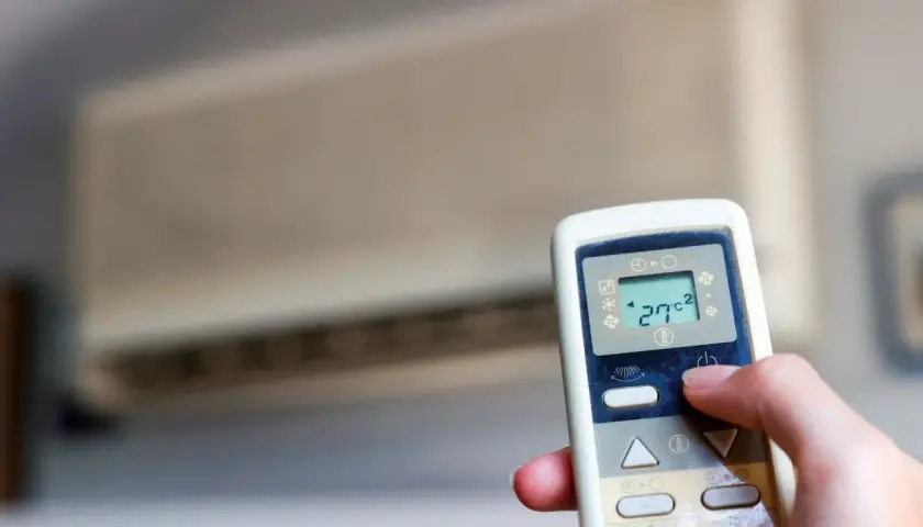 Mano ajustando el control remoto de un aire acondicionado cool o heat. La pantalla muestra 27°C.
