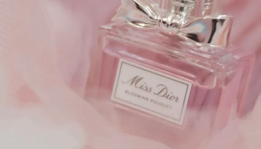 Frasco de perfume Miss Dior Blooming Bouquet, con un lazo plateado, sobre tela rosa suave. Un toque de elegancia para la madame de rosa.