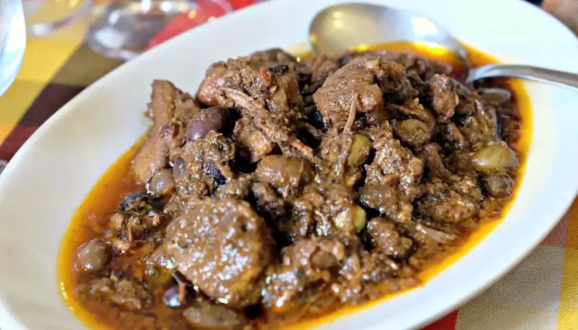 Un saporito cinghiale alla cacciatora, con olive e una ricca salsa, servito in un piatto bianco.