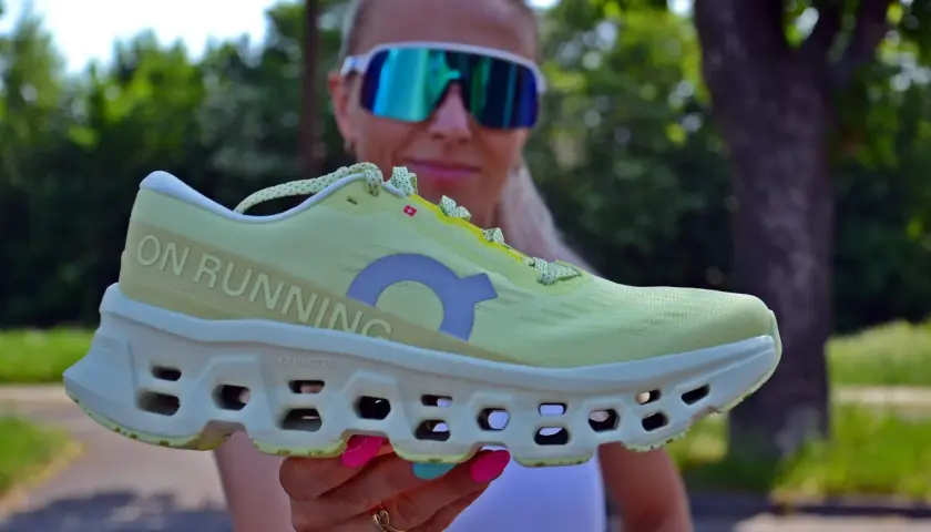 Kobieta w okularach przeciwsłonecznych prezentuje jasnożółty but do biegania z napisem "ON RUNNING". Czy w butach do biegania można chodzić? Tak, są wygodne!