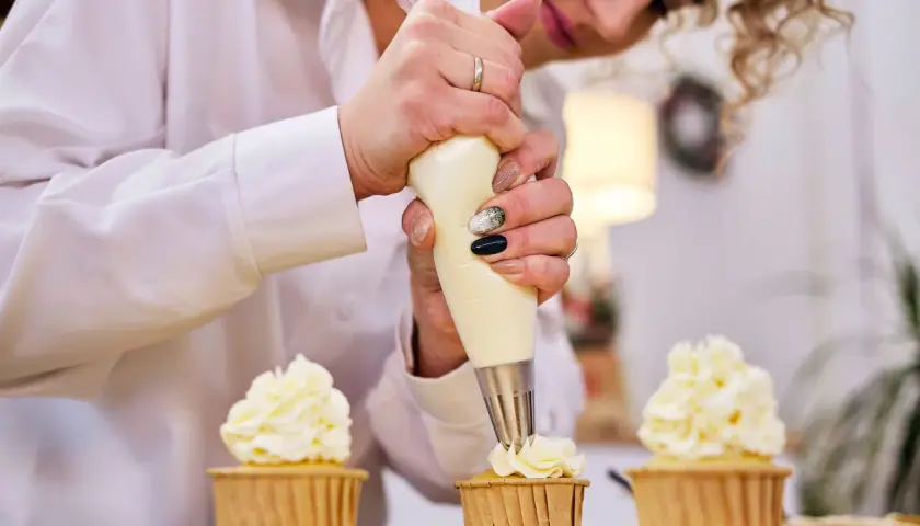 Pâtissière décorant des cupcakes avec une poche à douille. La crème est d'une belle couleur ivoire, parfaite pour savoir quel colorant pour chantilly mascarpone utiliser.