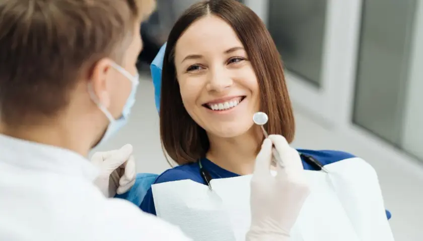 Uśmiechnięta pacjentka podczas wizyty u dentysty. Lekarz w masce i rękawiczkach bada jej zęby, przygotowując się do ewentualnego piłowania zębów.
