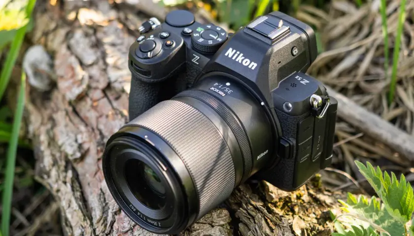 Aparat Nikon Z5 II z obiektywem Nikkor 35mm f/1.4 leży na spróchniałym drewnie, otoczony zielenią.