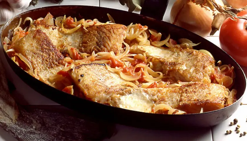 Morue à la lyonnaise, des filets de poisson dorés mijotant avec des oignons et des tomates dans une poêle.